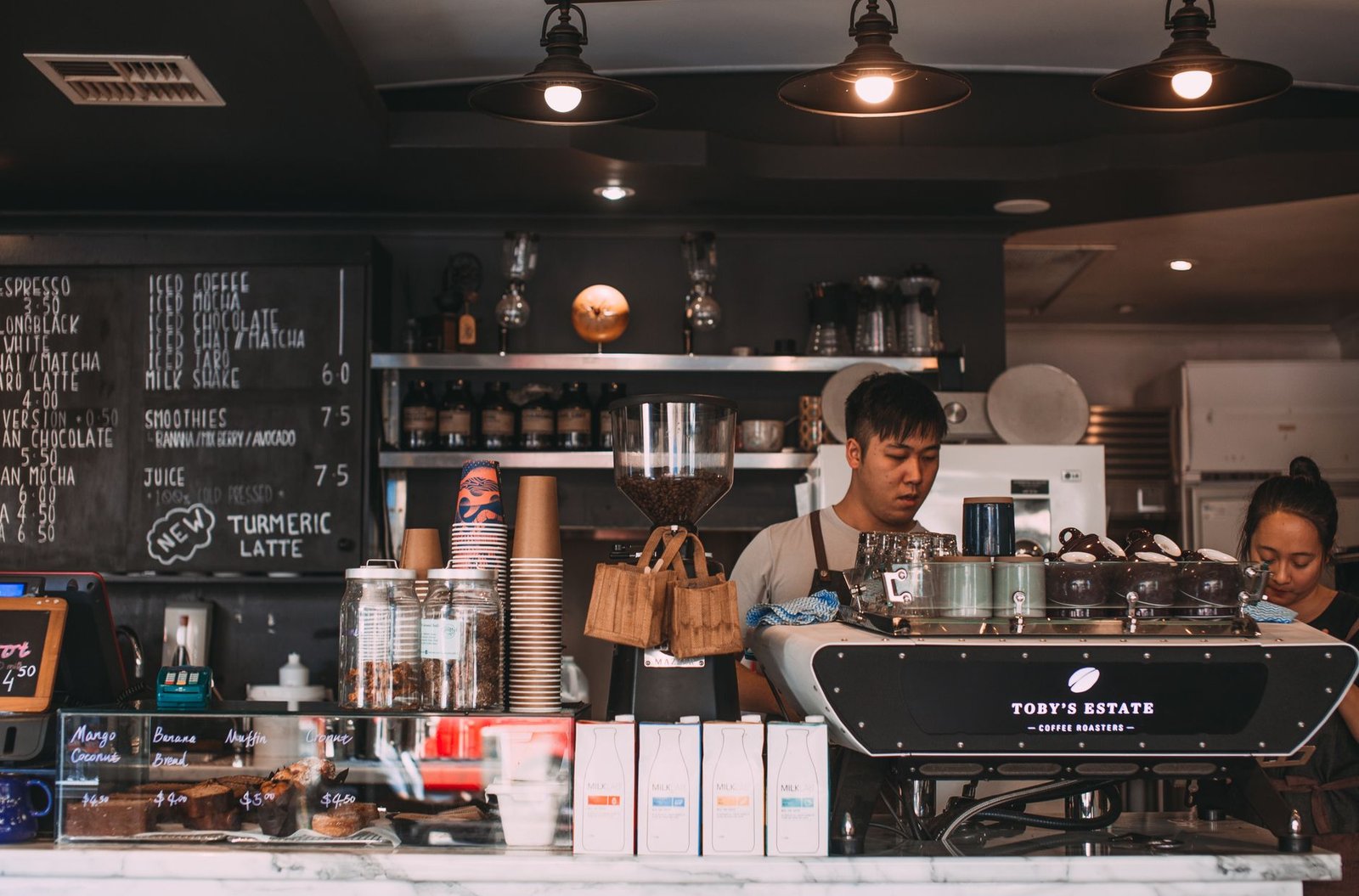 Comptoir de café avec machine à espresso et vitrine de pâtisseries.